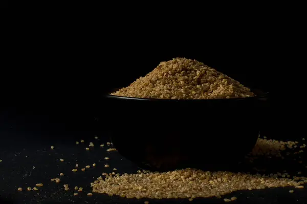 Сухая булгуровая пшеница в коричневой деревянной чаше, изолированная на темном дереве — стоковое фото