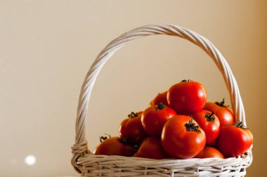 Ahşap masa üzerinde beyaz bir arka plan üzerinde dokuma sepet içinde kırmızı domates