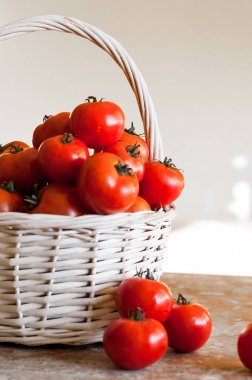 Ahşap masa üzerinde beyaz bir arka plan üzerinde dokuma sepet içinde kırmızı domates