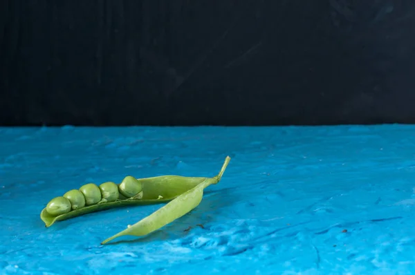 Jonge biologische groene erwt peulen en erwten op blauwe textuur achtergrond. Close-up. Oogst, gezond eten. — Stockfoto