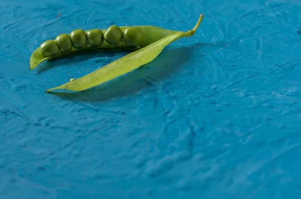 Jonge biologische groene erwt peulen en erwten op blauwe textuur achtergrond. Close-up. Oogst, gezond eten. — Stockfoto