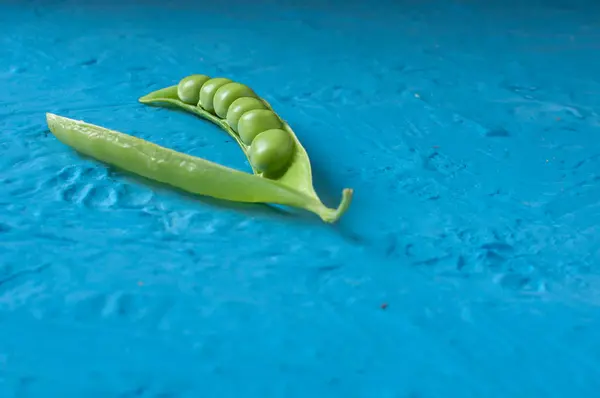 Jonge biologische groene erwt peulen en erwten op blauwe textuur achtergrond. Close-up. Oogst, gezond eten. — Stockfoto