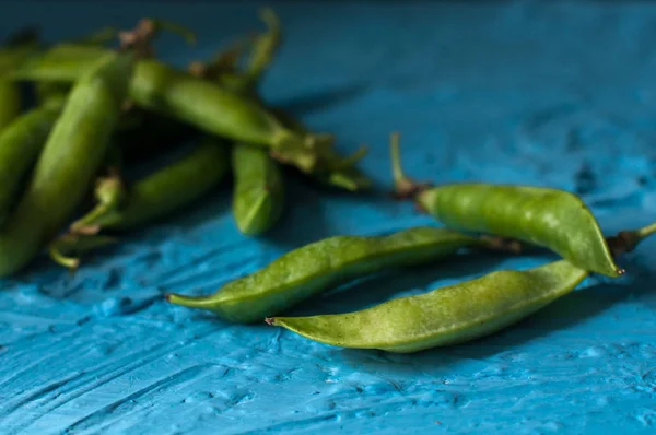 Jonge biologische groene erwt peulen en erwten op blauwe textuur achtergrond. Close-up. Oogst, gezond eten. — Stockfoto