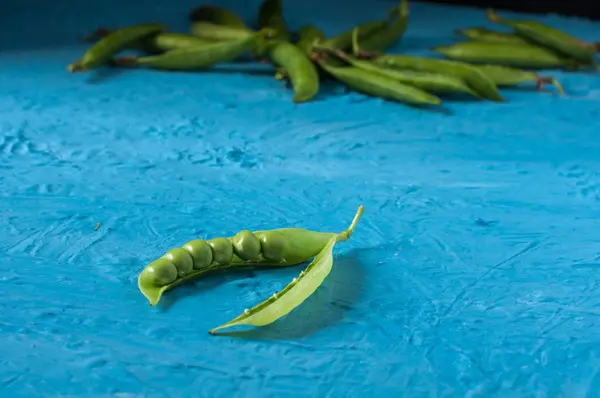 Jonge biologische groene erwt peulen en erwten op blauwe textuur achtergrond. Close-up. Oogst, gezond eten. — Stockfoto