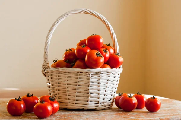 Rote Tomaten in einem geflochtenen Korb auf weißem Hintergrund auf einem Holztisch — Stockfoto
