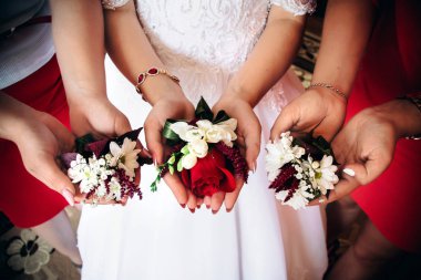 Düğün boutonies gelin ve sevgili elinde. Kırmızı gül ve papatya demetleri. Kızlar çiçek ellerini tutun..