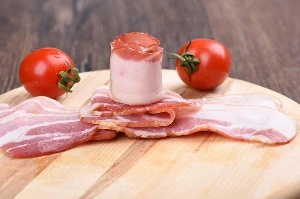 Rashers of bacon with cherry tomatoes on a cutting board.