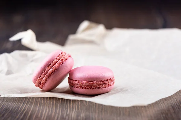 Två rosa makaroner på ett pappersark över en träbakgrund. — Stockfoto