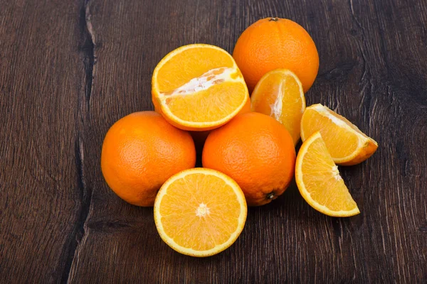 Naranjas, enteras y rebanadas, sobre una mesa de madera . — Foto de Stock