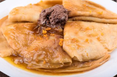 Makro atış. Beyaz tabakta tatlı soslu krep ve çikolatalı dondurma. Tahta bir masanın üzerinde krep tabağı.