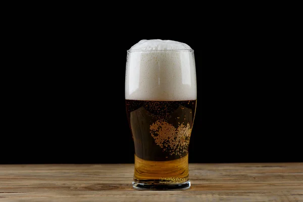 Glass of light beer with foam on a wooden table. Glass goblet with beer on a black background. Lager beer.