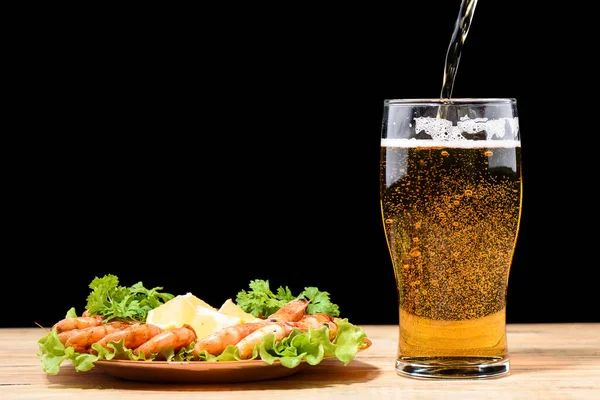 Light beer is poured into a beer glass. Plate with shrimp, lettuce and slices of lemon. Lager beer.
