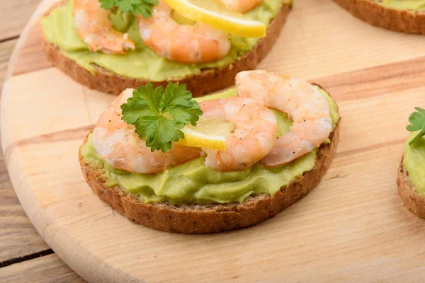 Sandwiches with avocado cream and shrimp on a cutting board. Multigrain bread, avocado cream, shrimp, lemon and parsley. Healthy eating.