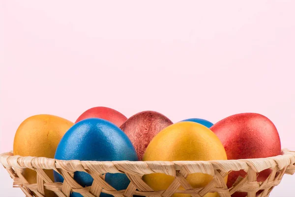 Корзина с разноцветными пасхальными яйцами на розовом фоне . — стоковое фото