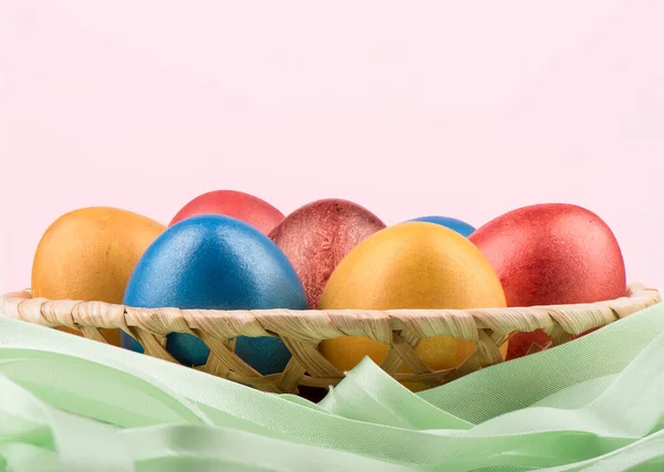 Корзина с разноцветными пасхальными яйцами и зеленой лентой на розовом фоне . — стоковое фото