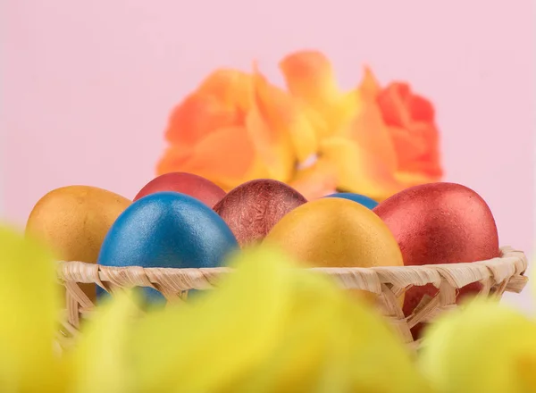 Выборочный фокус. Корзина с разноцветными пасхальными яйцами и размытыми цветами на переднем и заднем фоне . — стоковое фото