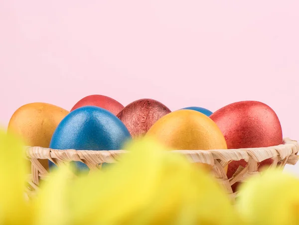 Выборочный фокус. Корзина с разноцветными пасхальными яйцами и размытыми желтыми цветами на переднем плане . — стоковое фото