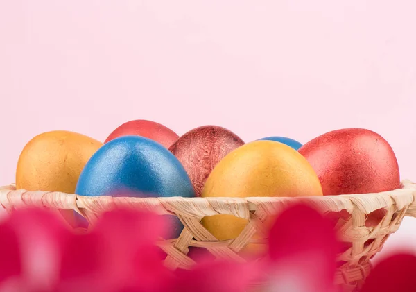 Выборочный фокус. Корзина с разноцветными пасхальными яйцами и размытыми красными цветами на переднем плане . — стоковое фото
