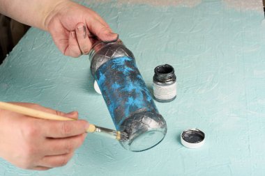 Cam bir kavanozu gri akrilik boyayla boyamak. Bir kadının elinde boya fırçası. Parmaklarda boya..