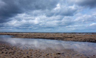 Bulutların yansıması bulutlu bir havada Jurmala 'da Baltık Denizi' nin kumlu kıyısında küçük bir lehman.