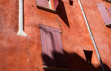 Eski şehirde kırmızı duvarları olan bir evin camlarında kırmızı panjurlar var.