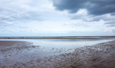 Bulutların yansıması bulutlu bir havada Jurmala 'da Baltık Denizi' nin kumlu kıyısında küçük bir lehman.