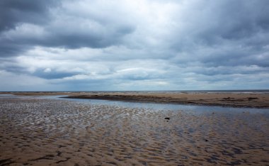 Bulutların yansıması bulutlu bir havada Jurmala 'da Baltık Denizi' nin kumlu kıyısında küçük bir lehman.
