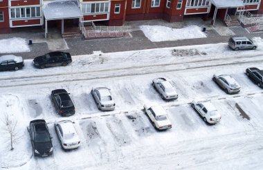 Kış mevsiminde çok katlı bir apartmanın avlusundaki karla kaplı arabaların üst görüntüsü..