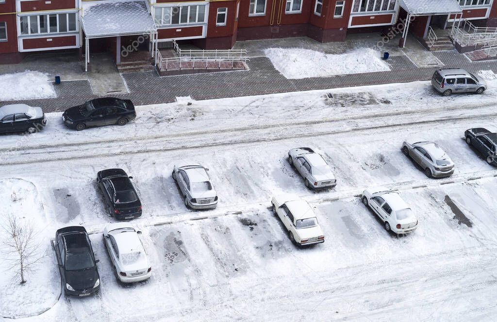 Top view of snow-covered parked cars in the courtyard of a multi-storey residential building in winter.