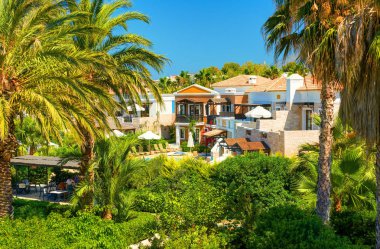 Girit Adası, Yunanistan, 01 Temmuz 2011: Turistler için otel villaları görünümü. Yeşil tropikal palmiye ağaçları yüzme havuzu, şezlong, şemsiye. Klasik mimari. Yunanistan ada tatili turları