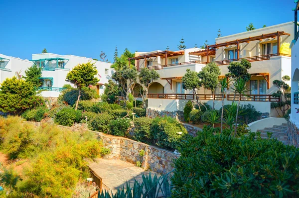 CRETE ISLAND, GREECE, SEP 08, 2012: Classical Greece hotel villa on stone beach among green trees for tourists guests. Arquitetura hoteleira grega de luxo. Grécia ilha férias passeios viagens. Panorama — Fotografia de Stock