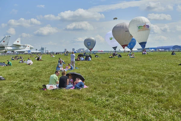 ZHUKOVSKY, Rusia, JUL. 21, 2017: Exposición aeronáutica MAKS 2017. Aerostatos globo de aire en aeródromo verde, la gente viendo espectáculo de aire Globos de aire caliente muestran en verano día soleado en el cielo azul nublado — Foto de Stock