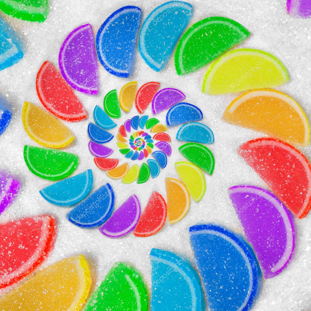 Abstract spiral fruit jelly rainbow wedges slices on white sugar sand background. Rainbow jelliy candies. Sweet fruit jelly liths. Candy dessert. Abstract food fractal Exotic sweets pattern background