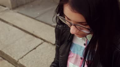 Güzel kız yakın çekim yüz. Kızın yüzü koyu saçlı, gözlük vizyon için. Kız telefon haberlerde bakar.