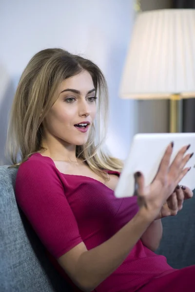 Tablet kullanarak kanepede oturan heyecanlı sevimli kadın