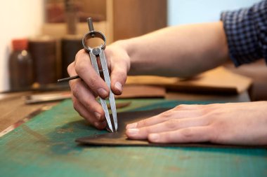 Zanaat araçları kullanılarak, doğal deri üzerindeki dikişin genişliğini ölçen ana kameraya yakın çekim. Sanatçının erkek eli, doğal derinin dikişlerinin genişliğini ölçüyor. Deri işçisinin çalışma süreci.