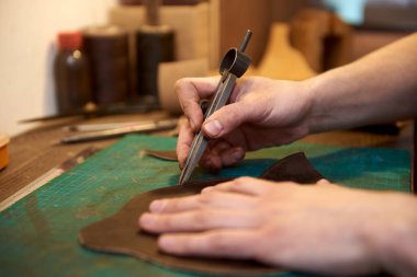 Sanatçının erkek eli, doğal derinin dikişlerinin genişliğini ölçüyor. Deri işçiliğinin çalışma süreci. Leatherman 'ın doğal deriyle çalışırken el işi aletleri kullandığı yakın plan..