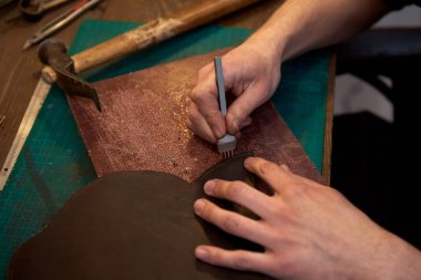 Deri adam el işi aleti tutuyor ve çalışma masasında hakiki deriyle çalışıyor. El işi aletleri kullanarak doğal deriyle çalışan zanaatkârların yakın çekimi. Hakiki deriyle çalışmak.