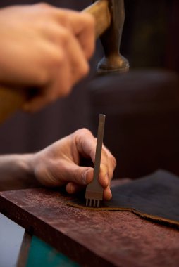 Zanaatkar çekiç ve ağızla gerçek deride küçük delikler açmak için çalışır. Deri yüzücü, el işi aletleri kullanarak kahverengi doğal deriyle çalışıyor..
