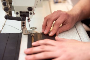 Deri işçisi atölyesinde dikiş makinesinde deri ürünler üretir. Erkek eller, beyaz dikiş makinesine gri deri cüzdan dikiyorlar. Manufactory ve deri adamın küçük işletmeleri.