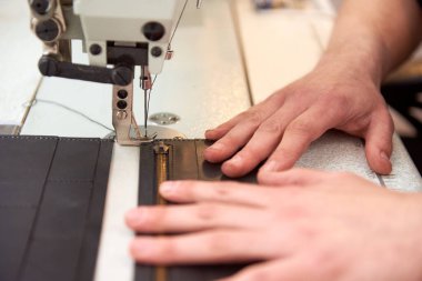 Deri işçisi atölyesinde dikiş makinesinde deri ürünler üretir. Erkek eller, beyaz dikiş makinesine gri deri cüzdan dikiyorlar. Manufactory ve deri adamın küçük işletmeleri.