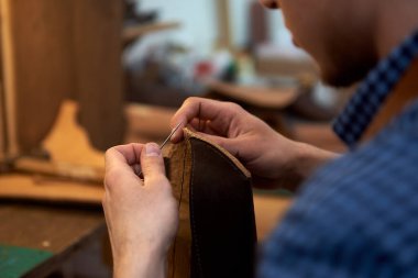 İleride gözlük takmak için kahverengi deri parçaları iğneyle diken zanaatkâr ellerinin yakın çekimi. Atölyesinde deri diken adam. Esnaf kahverengi deri, iğne ve iplikle çalışıyor. Küçük bir zanaatkar işi. Manufactory