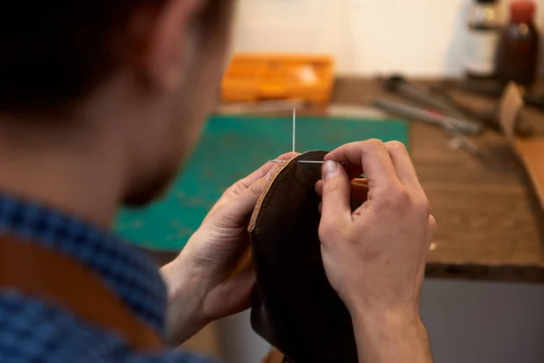 職人の手の閉鎖は メガネのための将来のケースのための針で茶色の革の部品を縫製 工房では針縫いの革を持った男 職人は茶色の革 糸で作業します 写真は 針仕事に使用することができます — ストック写真