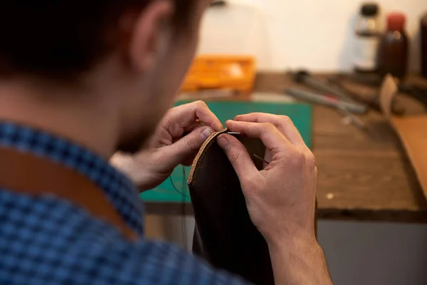 革の仕事のための革の男の糸針 男性の手の針で革の部分を縫製の閉鎖 主人は自分の机で革製品を作っている 本革の達人の手に糸を持った針の喪失 — ストック写真