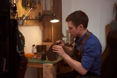 Usta, atölyesinde gelecekteki deri ürünlerinin düzeniyle çalışıyor. Manufactory ve deri adamın küçük işletmeleri. Fotoğraf, dikiş, el işi, deri ürünleri, hobiler, el yapımı ürünler, kendi mekanizması için kullanılabilir.