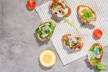 Gri beton veya taş zemin üzerine somon balığı, domates, peynir ve fesleğen pesto ile İtalyan bruschetta.