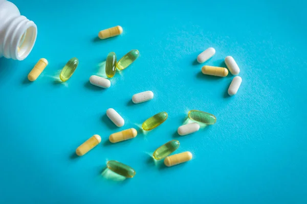 Omega capsules and vitamins scattered from a jar on a blue background. Photo with soft focus, macro shot.