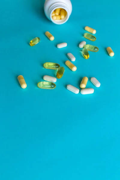 Vitamins and pills on a blue background in rows with a pill box. Omega Capsules and White Yellow Vitamins. Photo with soft focus, macro shot.