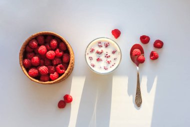 Beyaz arka planda bir fincan sütle kasede ahududu. Üst görünüm