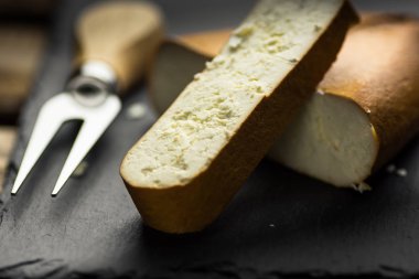 Siyah taş kurulu füme keçi peyniri yığın ve kesilmiş kalın bir dilim, çatal ve bıçak arka planda